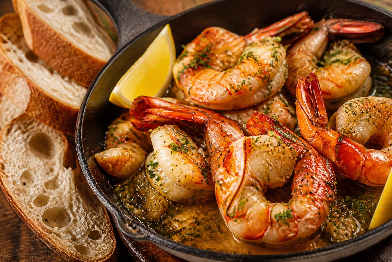 Giant prawns in garlic butter sauce in a cast iron pan with parsley and crusty bread